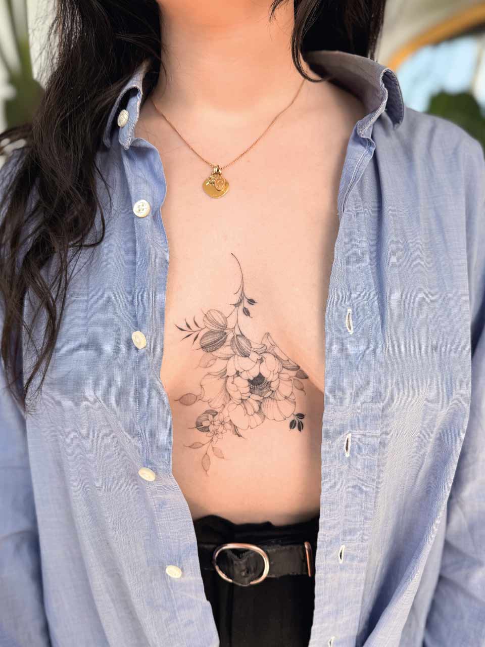 tatouage entre les seins d'une fleur délicate et fine en noir et gris